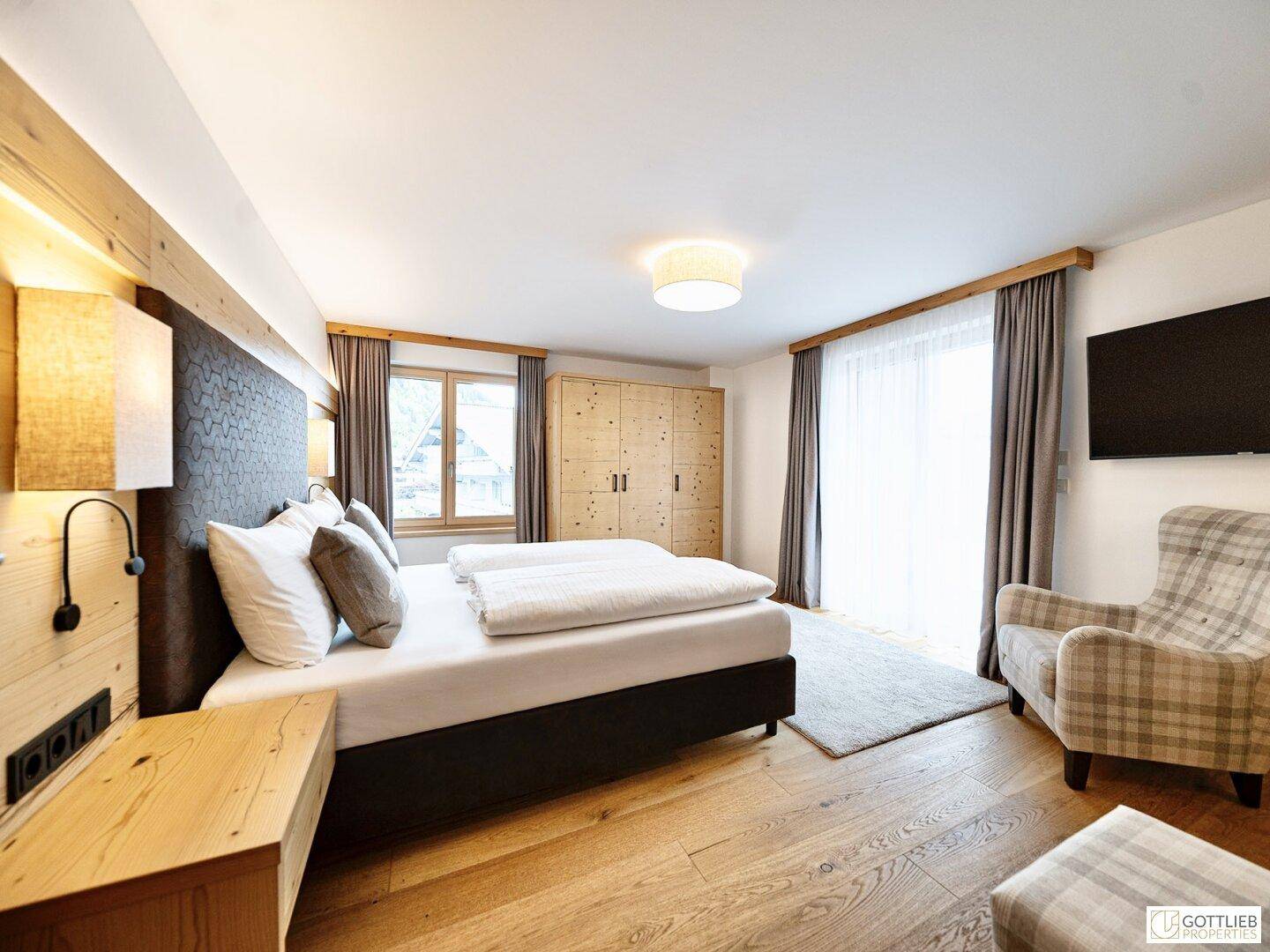 Gemütliches Schlafzimmer mit Doppelbett, Holzwand und bequemen Sessel, mit Zugang nach draußen.