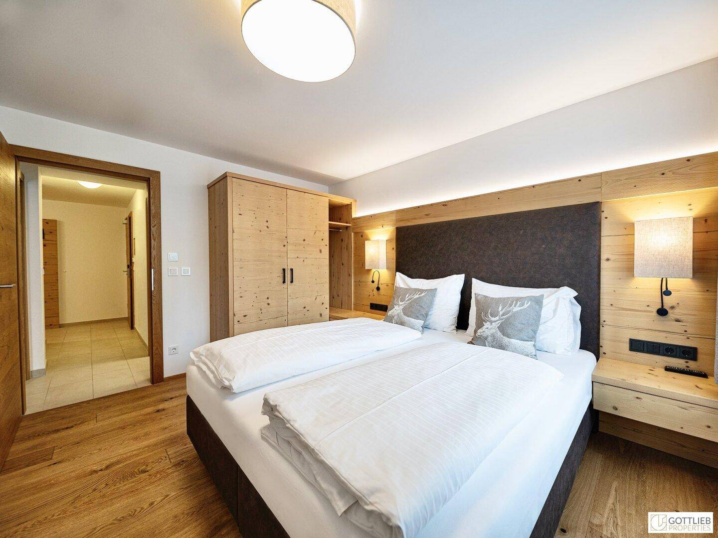 Helles Schlafzimmer mit Doppelbett, Holzwand und großem Holzschrank, mit Zugang zum Flur.