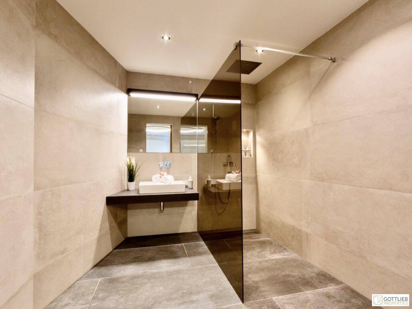 Modernes Badezimmer mit begehbarer Dusche, stilvollem Waschbecken und großformatigen Fliesen.