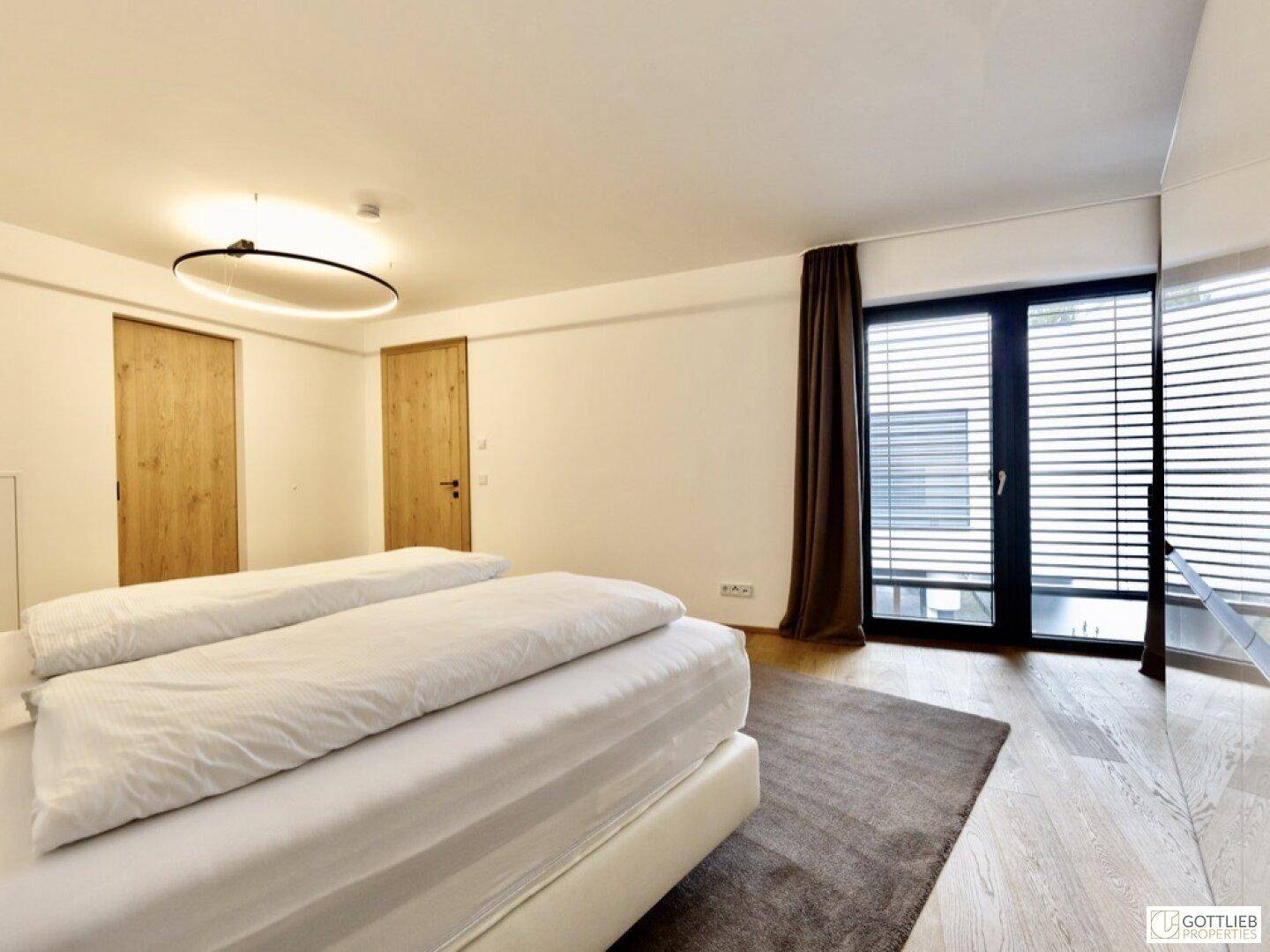 Helles Schlafzimmer mit Doppelbett, Holzboden und Zugang zu einem Balkon oder Terrasse.