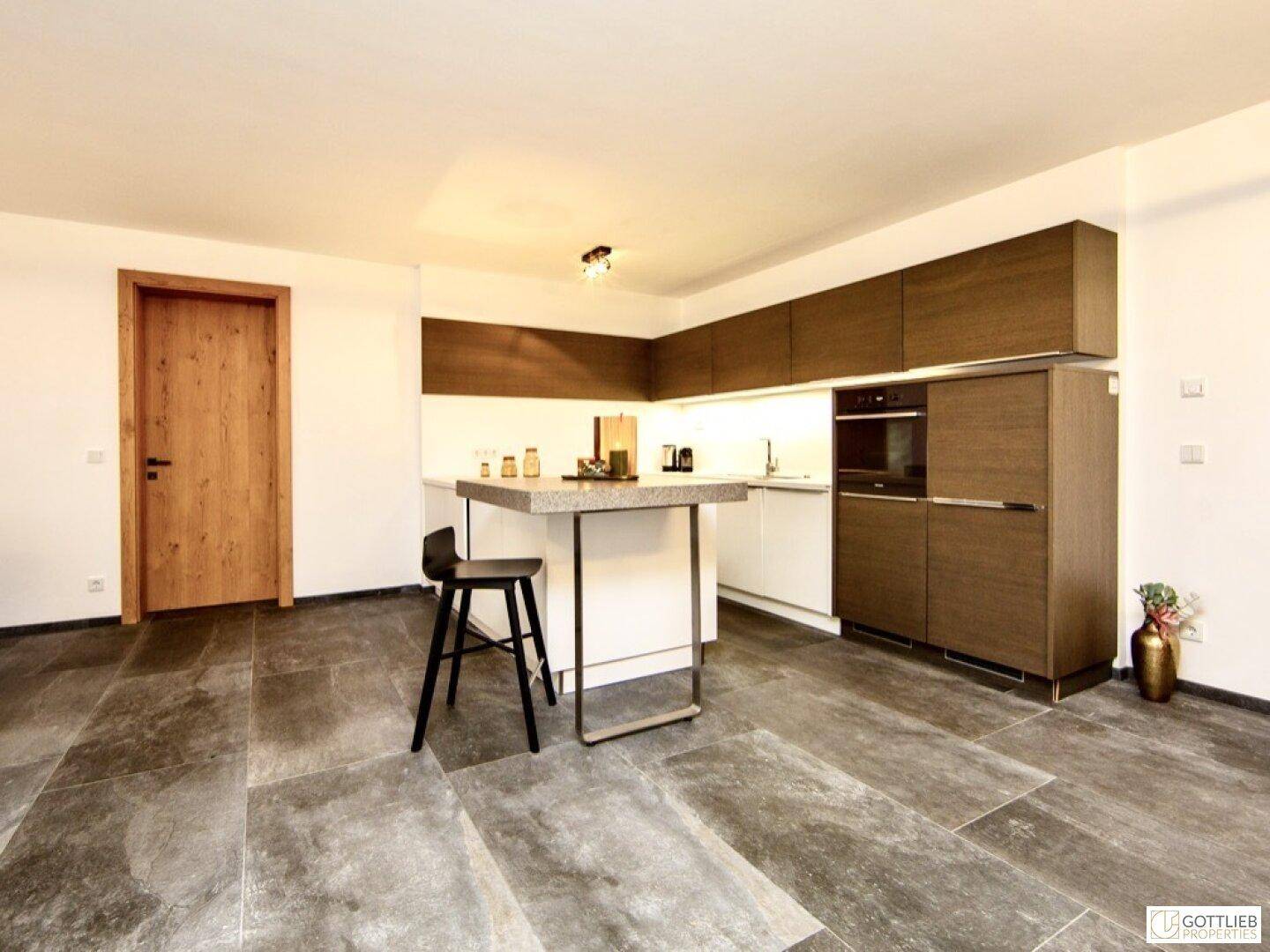 Moderne Küche mit weißen und holzfarbenen Schränken, einer Frühstücksbar und Fliesenboden.