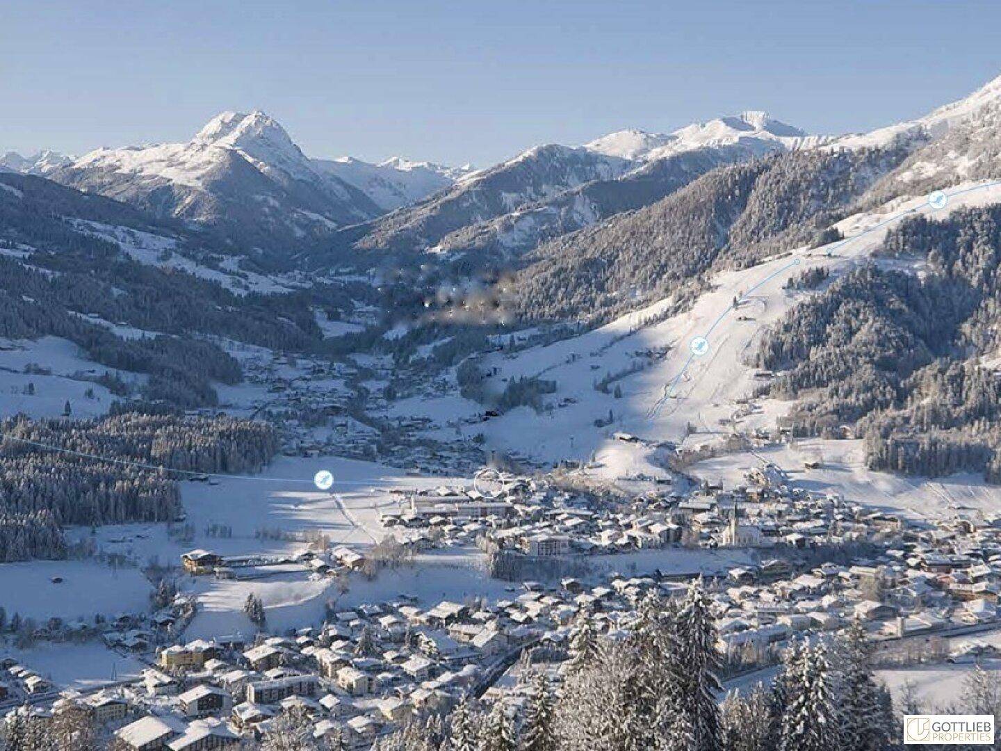 Panoramablick auf ein verschneites Tal mit einem Dorf und Skipisten in den Bergen.