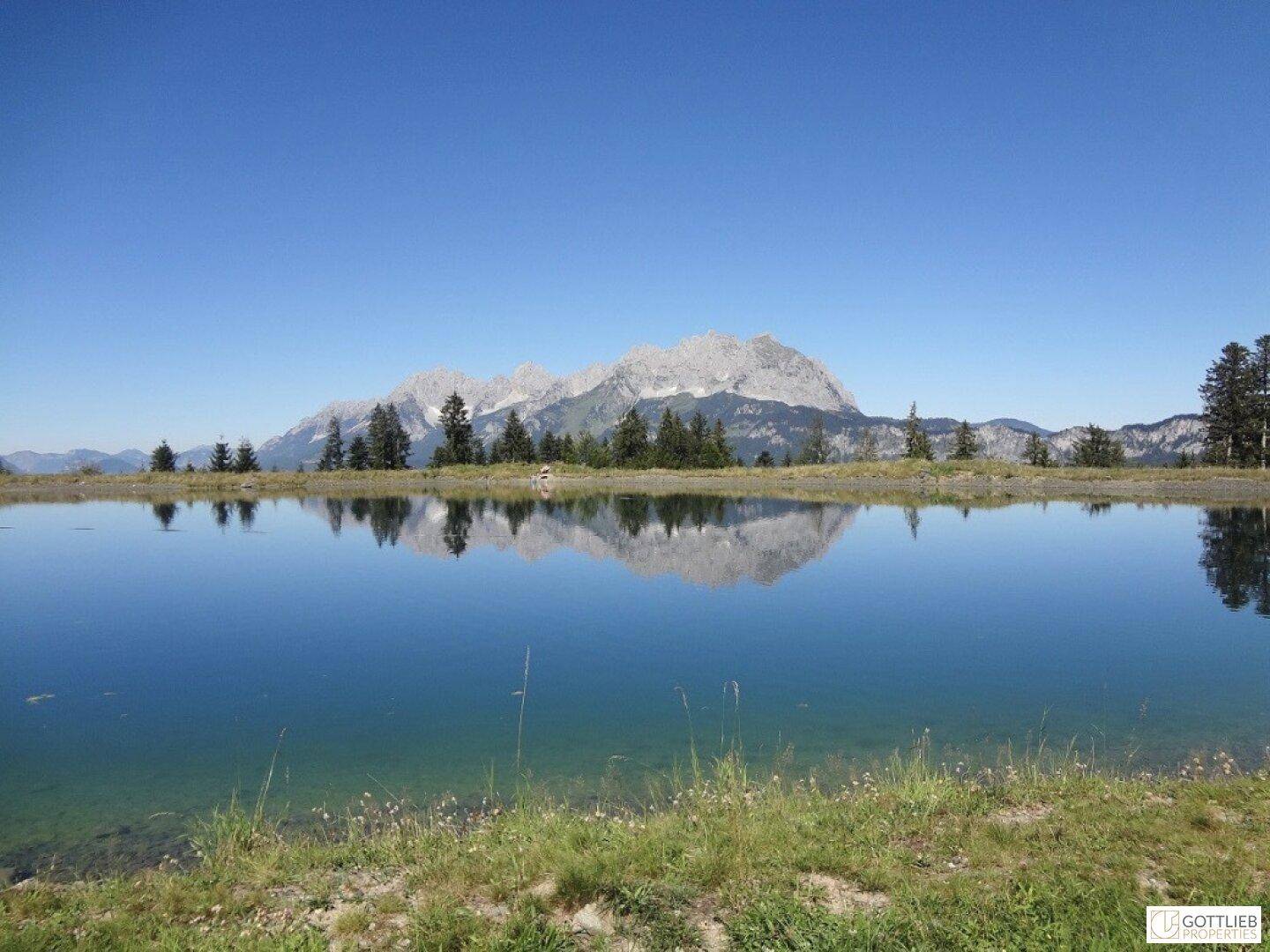 Idyllischer Bergsee mit klarer Wasseroberfläche und majestätischen Gipfeln im Hintergrund.