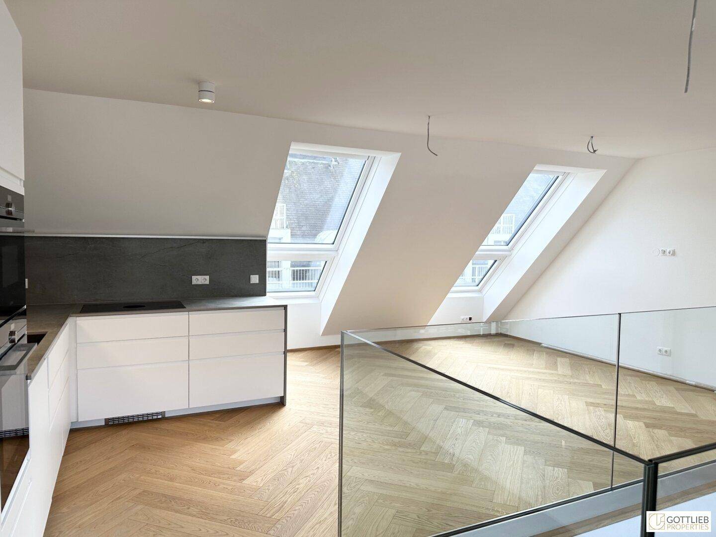 Heller offener Wohnbereich mit Dachschrägen, Fischgrätparkett und moderner Küche im Dachgeschoss.