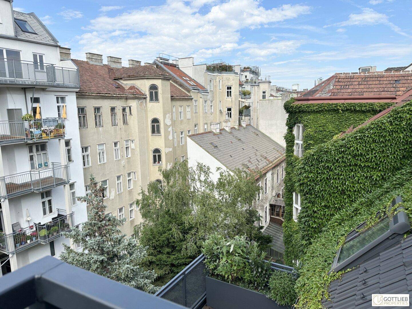 Ausblick von einem Balkon auf die umliegenden Gebäude und grüne Bäume in der Nachbarschaft.
