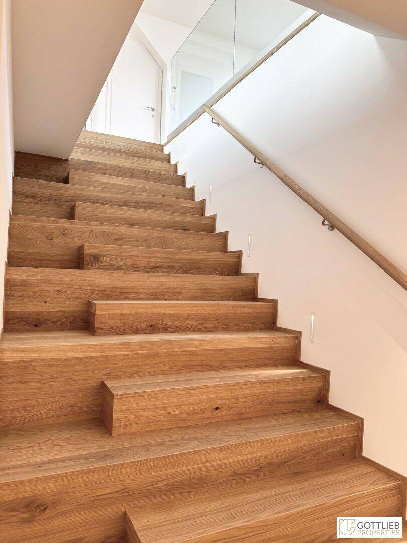 Elegante Holztreppe mit Glasgeländer und integrierter Beleuchtung, die die Etagen verbindet.