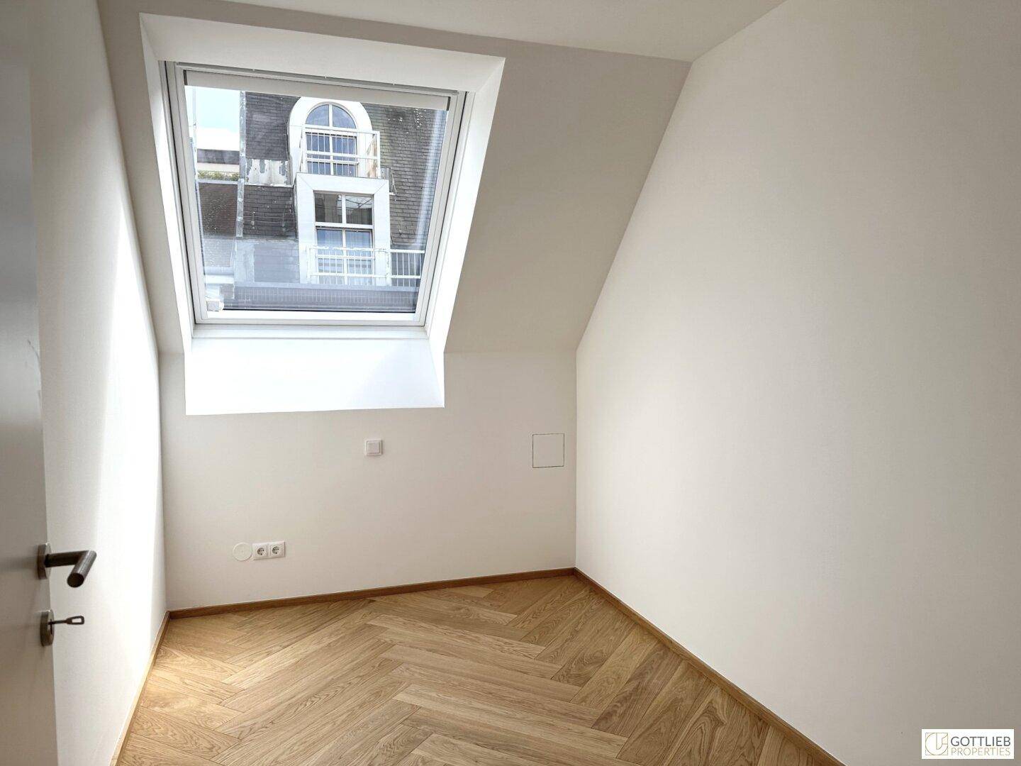 Helles Zimmer im Dachgeschoss mit schrägen Wänden, Dachfenster und Fischgrätparkett.
