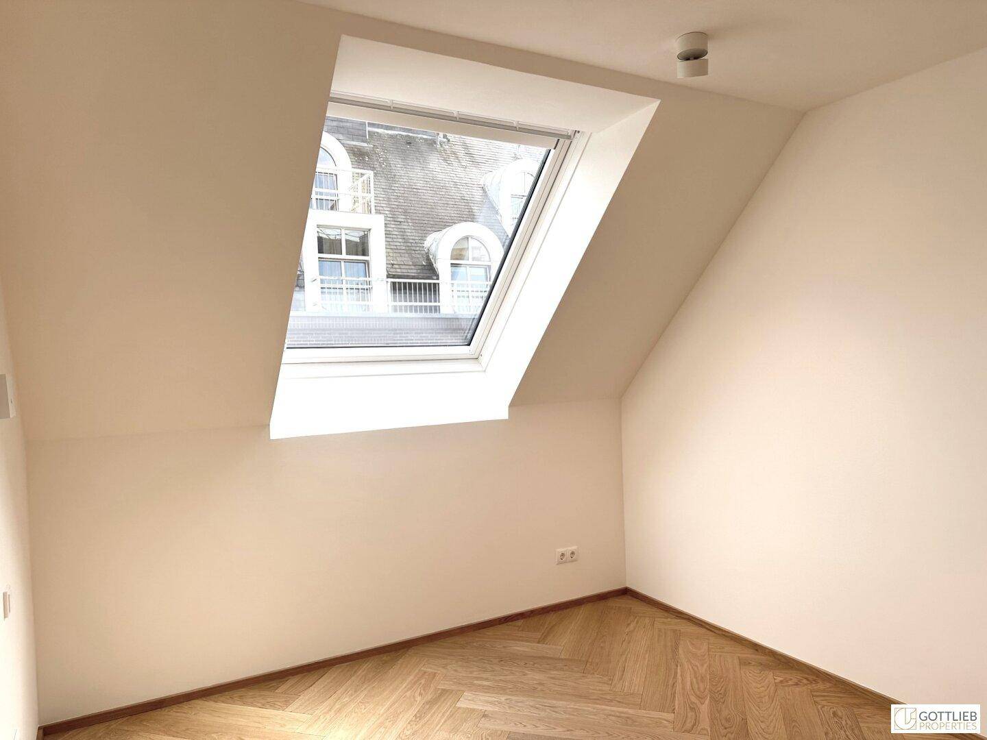 Kleines, helles Zimmer mit Dachschräge, Dachfenster und moderner Deckenbeleuchtung.
