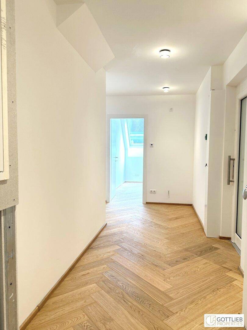 Heller Flur mit Fischgrätparkett und weiß gestrichenen Wänden, der zu weiteren Räumen führt.