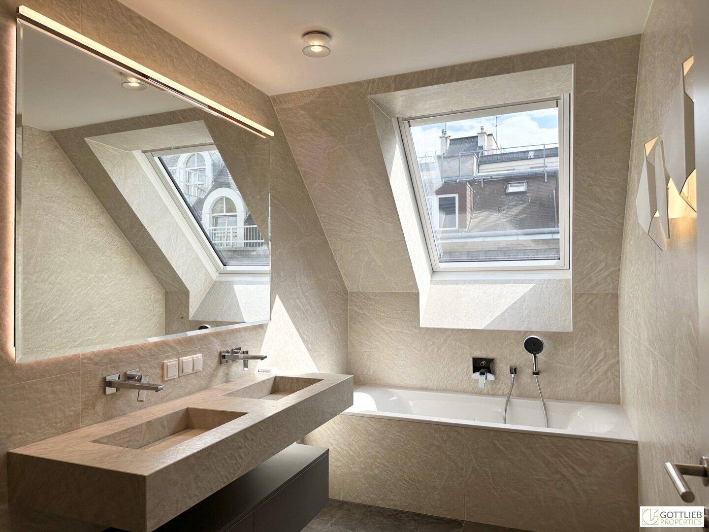 Modernes Badezimmer mit Doppelwaschbecken, Badewanne unter Dachfenster und eleganten Fliesen.