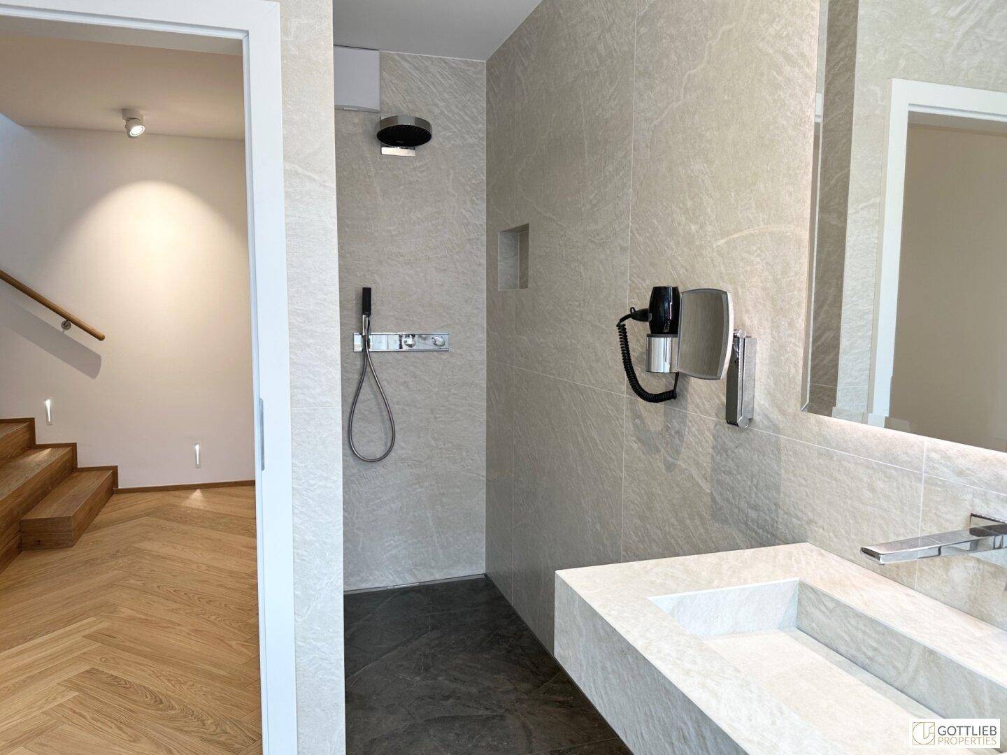 Modernes Badezimmer mit begehbarer Dusche, Einzelwaschbecken und Holzparkett im angrenzenden Flur.