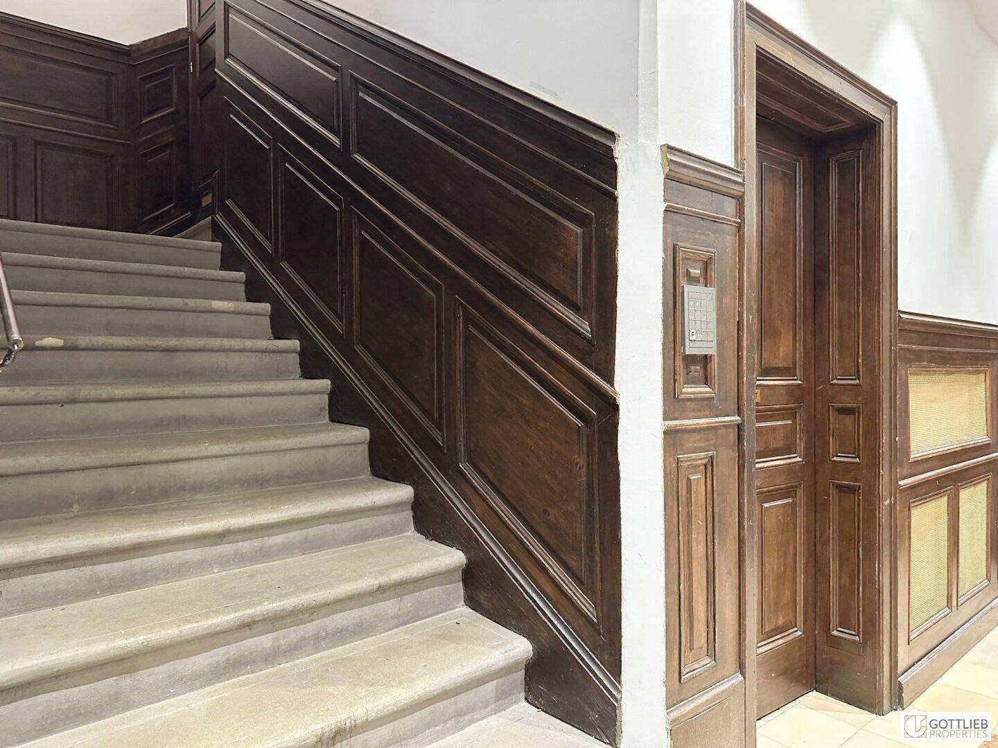 Treppenhaus mit Holzvertäfelung und Zugang zum Aufzug.
