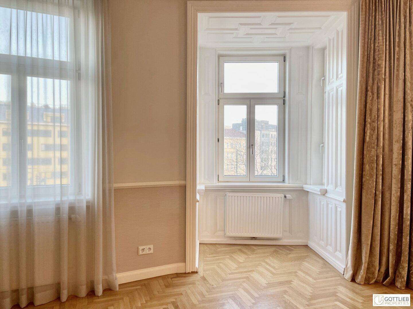 Heller Raum mit Fischgrätparkett, hohen Fenstern und klassischer Wandvertäfelung, bereit zur Einrichtung.