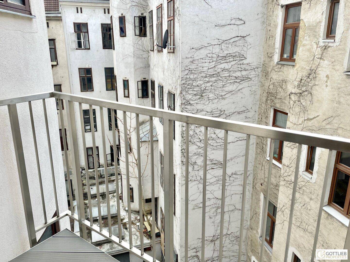 Balkon mit Blick auf einen ruhigen Innenhof, umgeben von historischen Gebäuden mit vielen Fenstern.