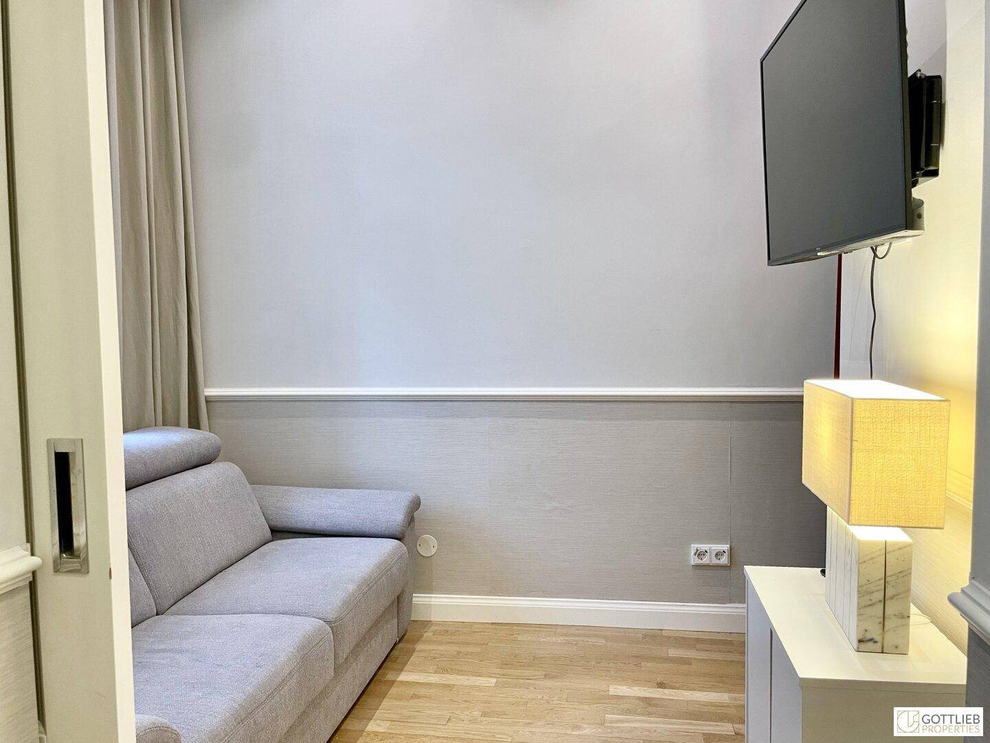 Kleiner Wohnbereich mit modernem Sofa, Wandfernseher und stilvoller Beleuchtung, ideal für Entspannung.
