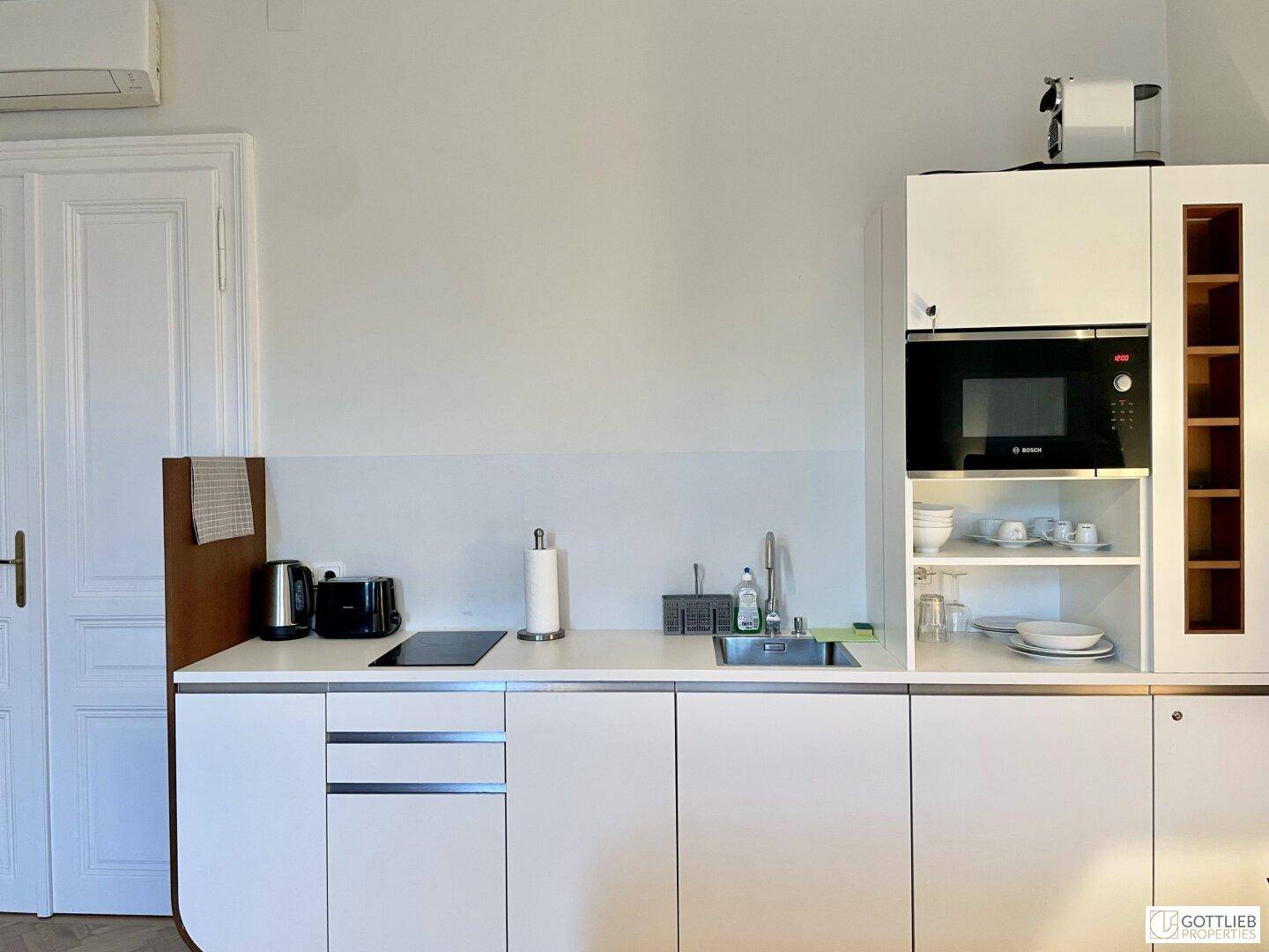 Kompakte, moderne Küchenzeile mit weißen Schränken, integrierter Mikrowelle und Induktionskochfeld.