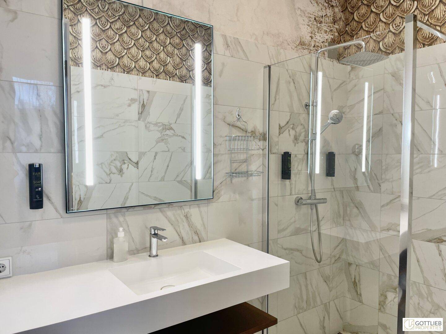 Elegantes Badezimmer mit großer begehbarer Dusche, modernem Waschtisch und beleuchtetem Spiegel.