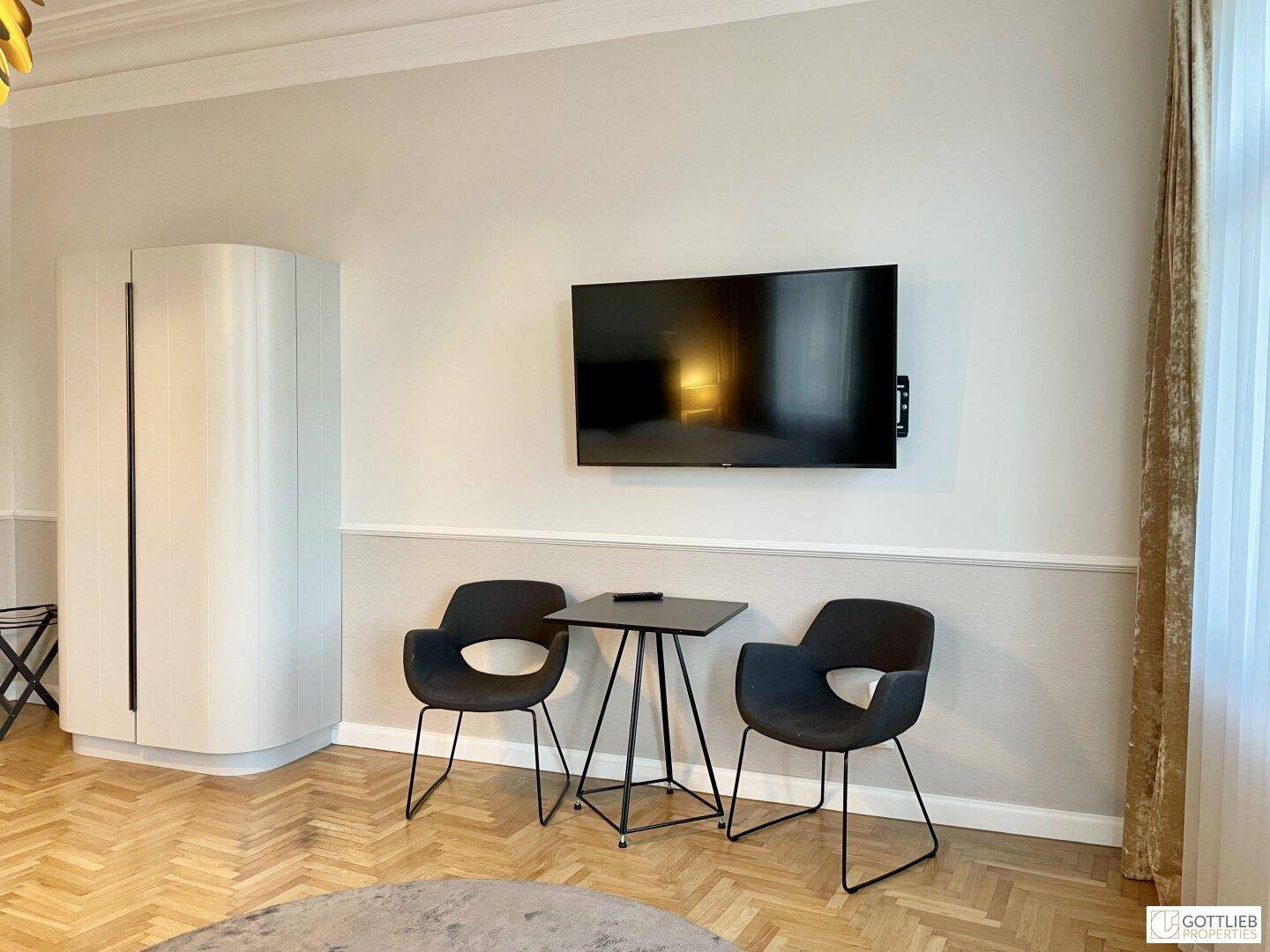 Vielseitiger Raum mit Wandfernseher, Sitzgelegenheiten und modernem Schrank, ideal für verschiedene Nutzungen.
