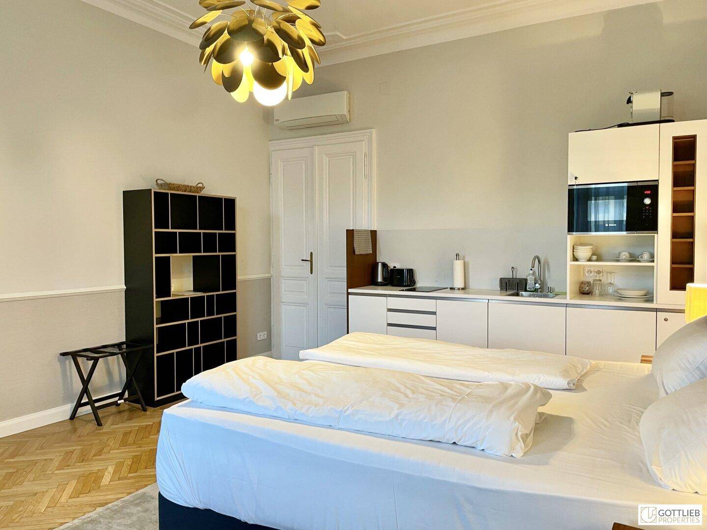 Modernes Studio-Apartment mit Schlafbereich, kompakter Küchenzeile und praktischem Regal für Stauraum.