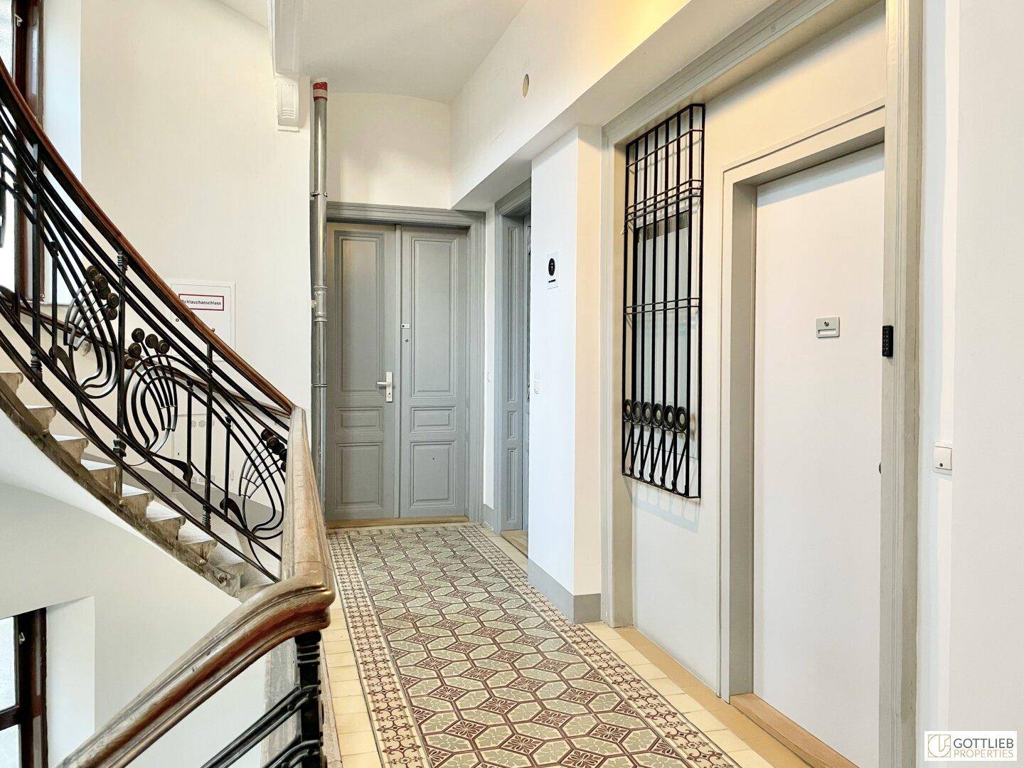 Historischer Flur mit gemusterten Fliesen, einer eleganten Treppe und mehreren Türen in einem Altbau.