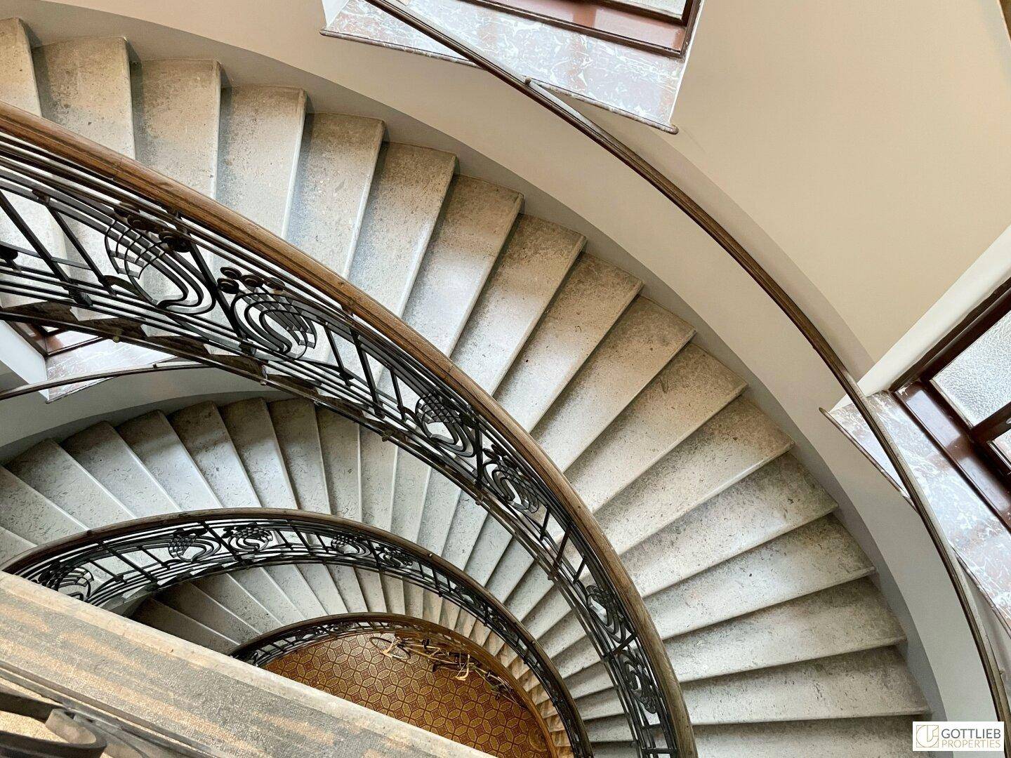 Elegante Wendeltreppe in einem historischen Gebäude, mit kunstvollem Geländer und Steinstufen.
