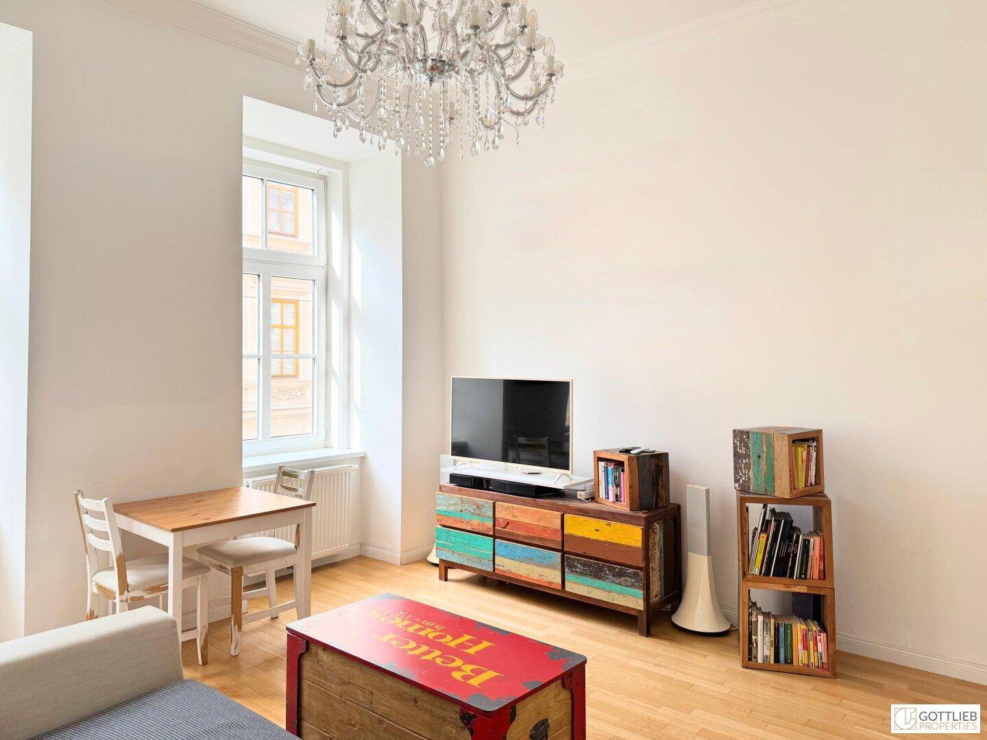 Wohnzimmer mit Holzboden, Fernseher auf einem bunten Sideboard und einem kleinen Esstisch.