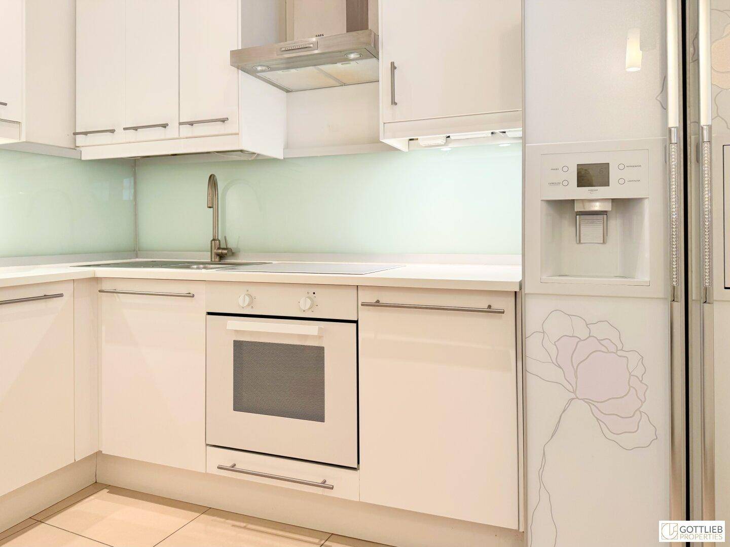 Moderne weiße Küche mit integrierten Geräten, Dunstabzugshaube und floralem Kühlschrankdesign.