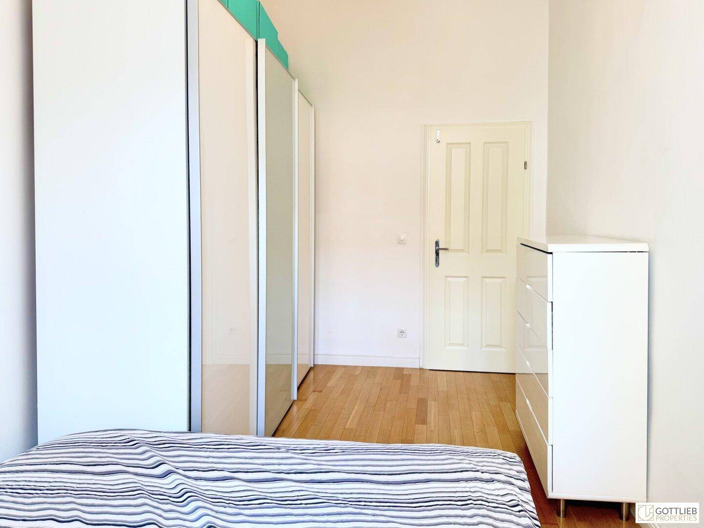 Schlafzimmer mit Holzboden, weißen Kleiderschränken und einer Kommode.