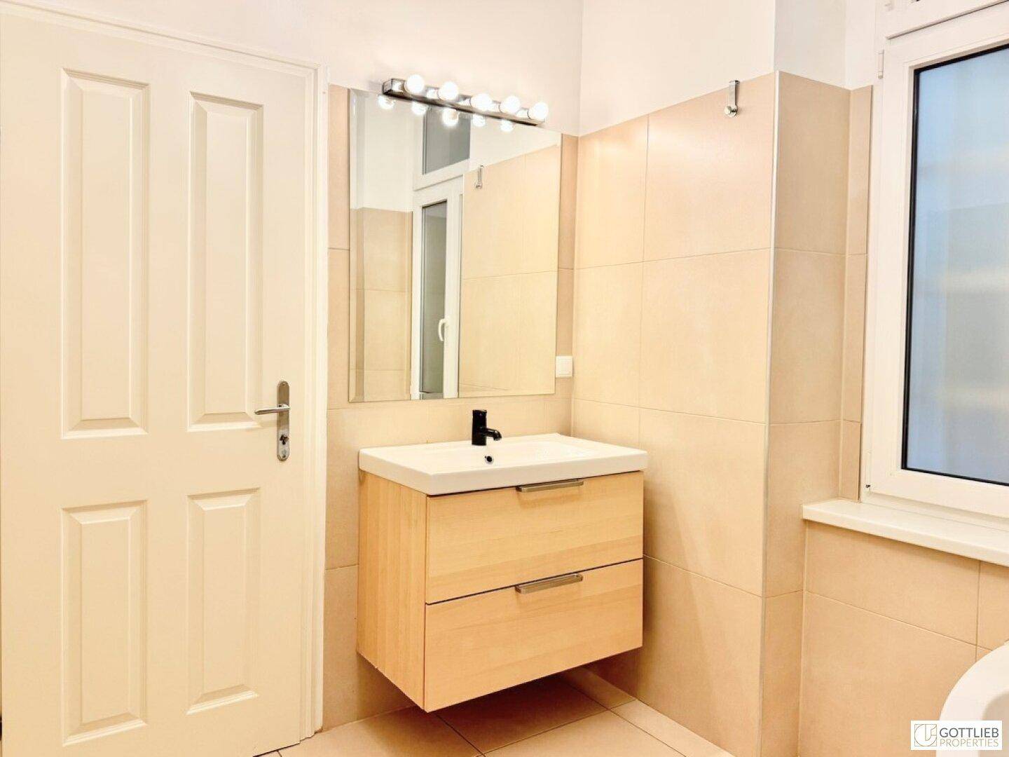 Modernes Badezimmer mit hellem Holzwaschtisch, Spiegel und Fenster.