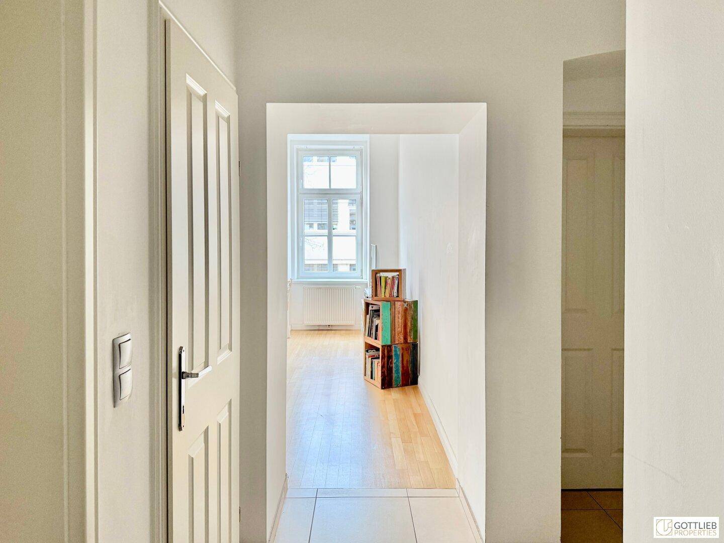 Heller Flur mit Fliesenboden, der zu einem weiteren Raum mit Holzboden führt.