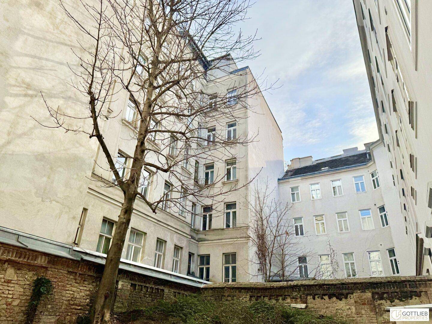 Innenhof eines Altbaus mit Bäumen und einer Ziegelmauer.