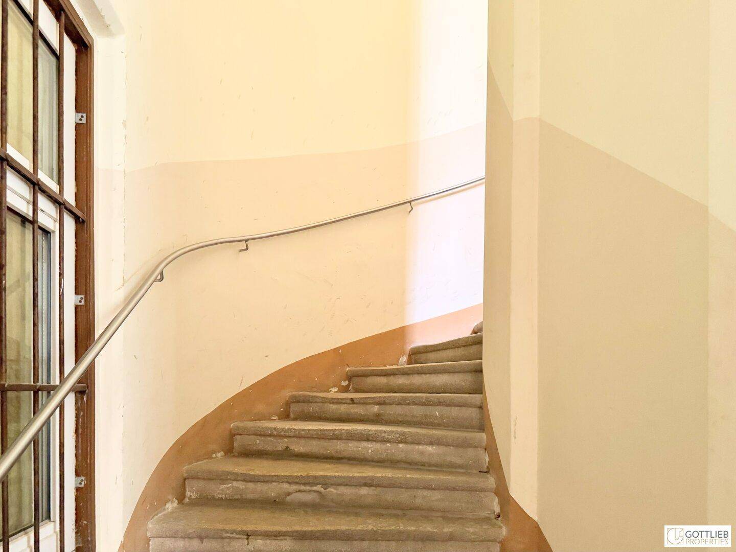 Treppenhaus mit Steinstufen und einem Handlauf in einem Altbau.