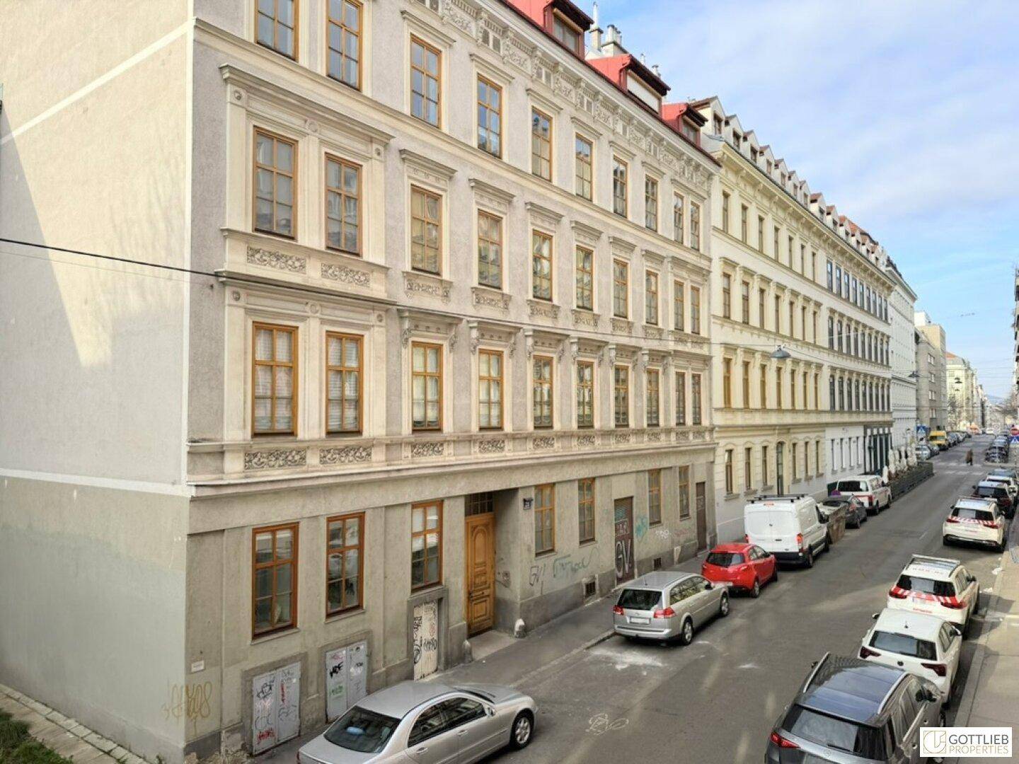 Historisches Gebäude an einer Straße mit parkenden Autos und vielen Fenstern.