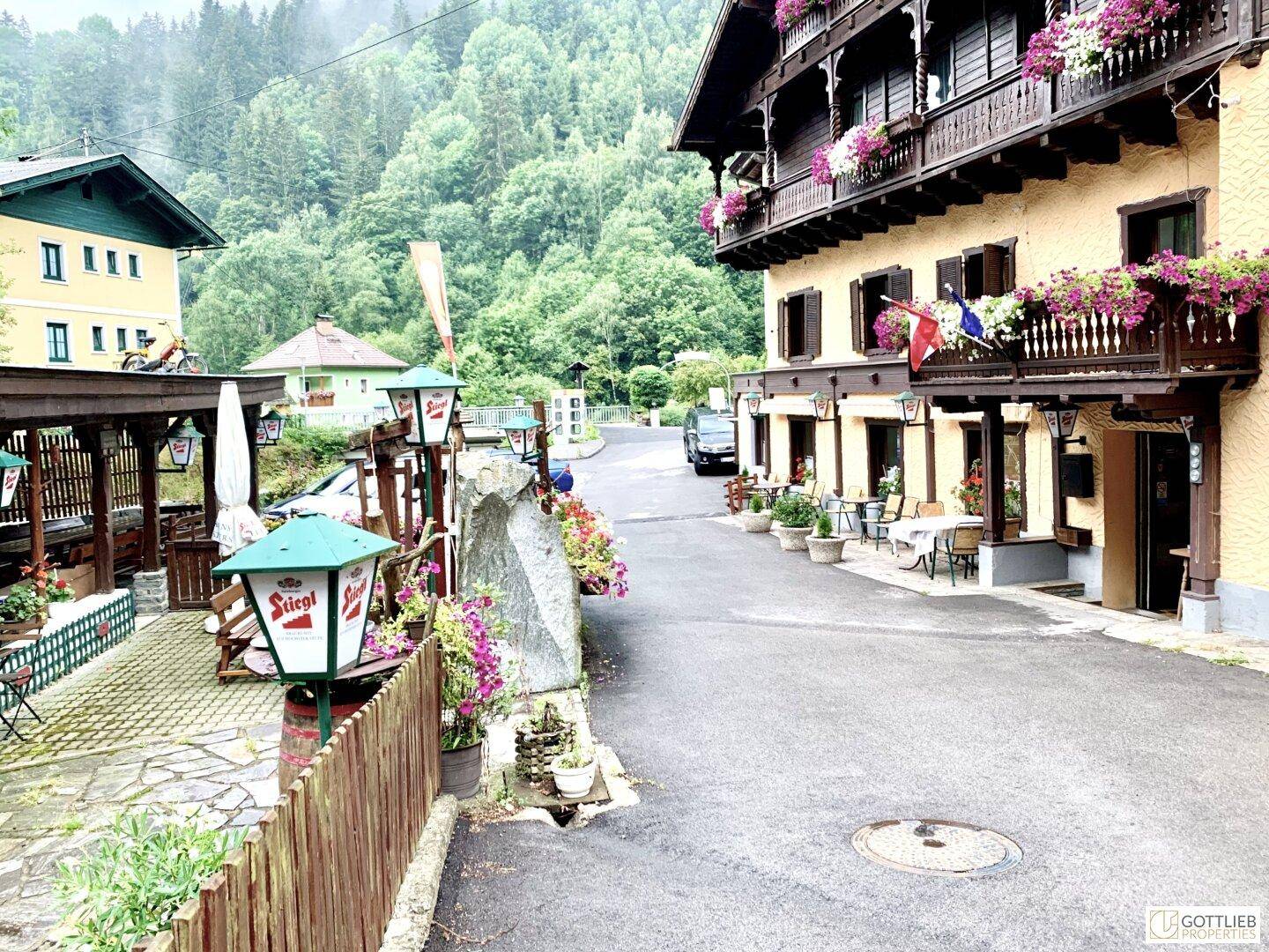 Traditionelle Gebäude entlang einer Straße mit Außensitzbereichen und Blumenkästen in bergiger Umgebung.