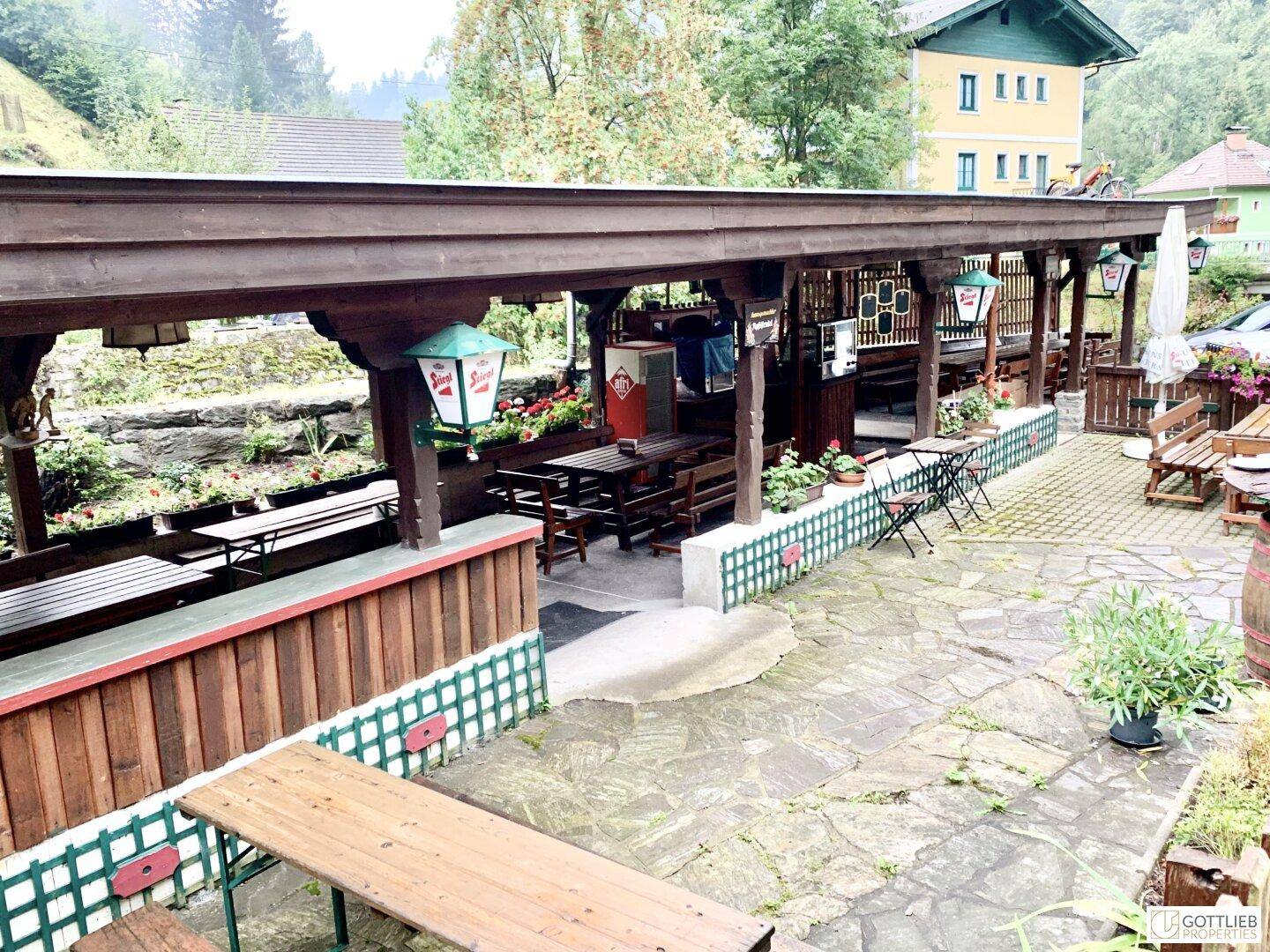 Überdachter Außenbereich mit Holzbänken und Tischen, ideal für gesellige Runden im Freien.