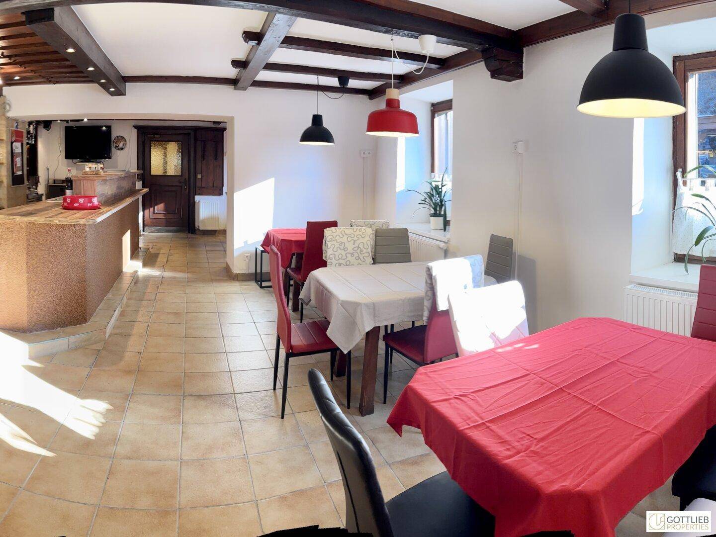 Gemütlicher Speisesaal mit traditionellen Holzbalken, roten Tischdecken und rustikalem Charme.