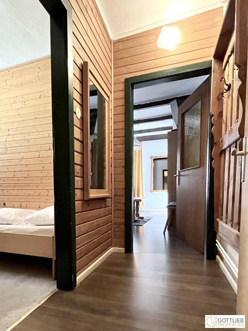 Schmaler Flur mit Holzverkleidung, der zu einem Schlafzimmer mit Holzboden führt.