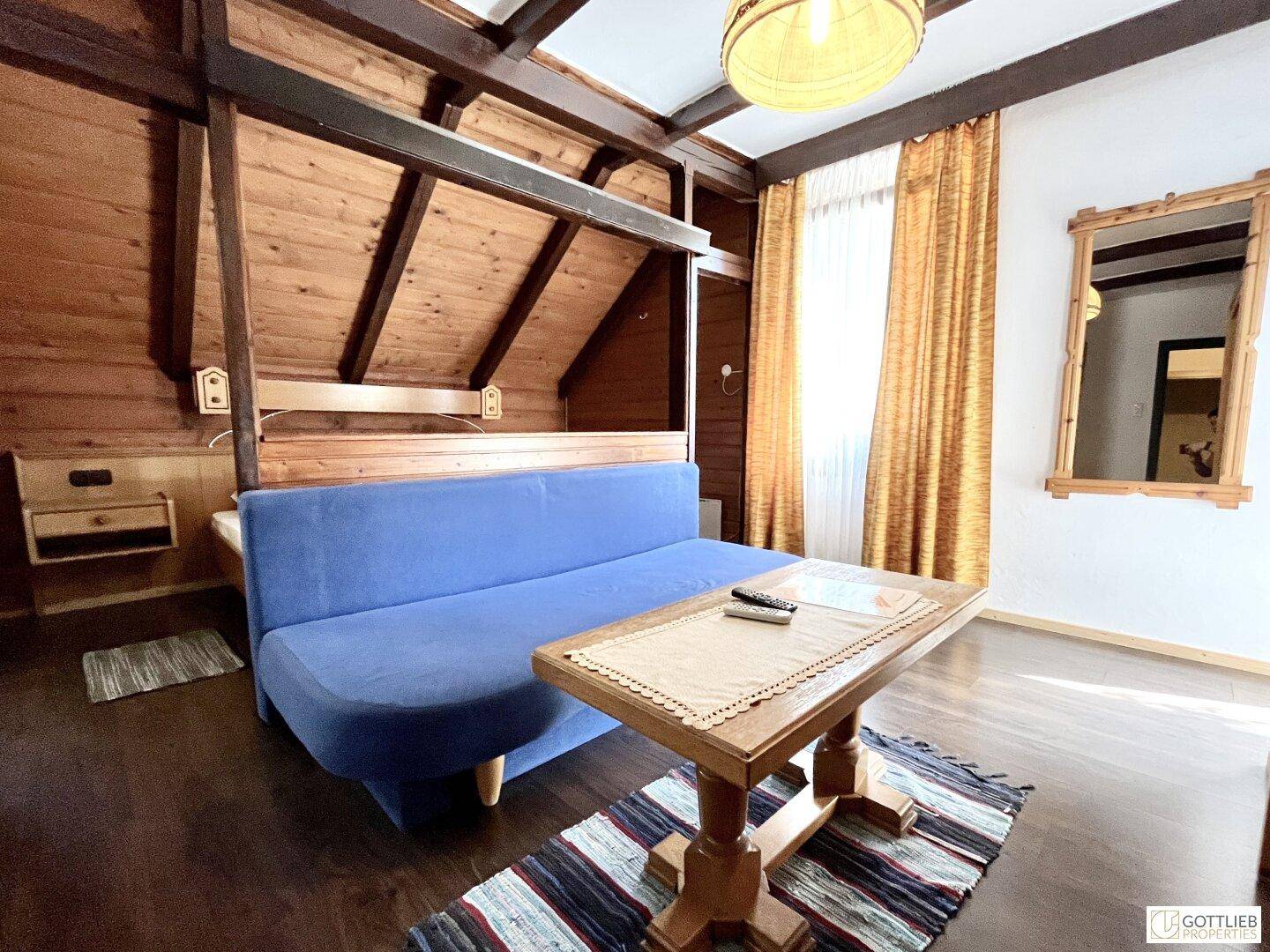 Gemütliches Schlafzimmer mit Holzwänden, einem blauen Sofa und einem Holztisch unter Dachschrägen.