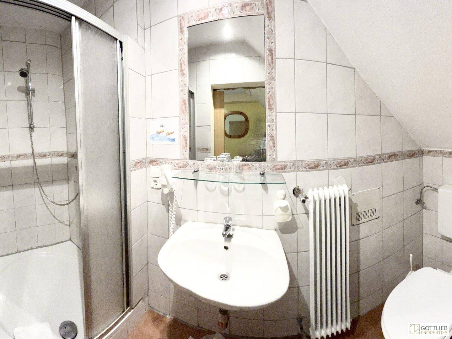 Helles Badezimmer mit Duschkabine, Waschbecken und WC, ausgestattet mit weißen Fliesen und Dachschräge.