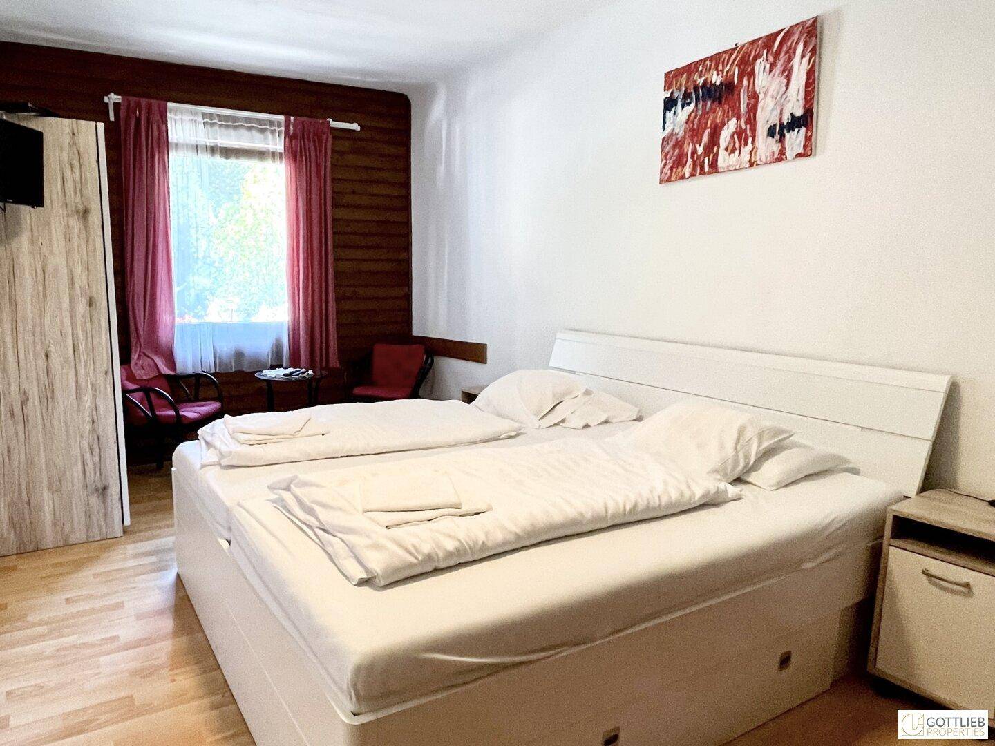 Geräumiges Schlafzimmer mit Doppelbett, Holzboden und großem Fenster, das viel Tageslicht hereinlässt.