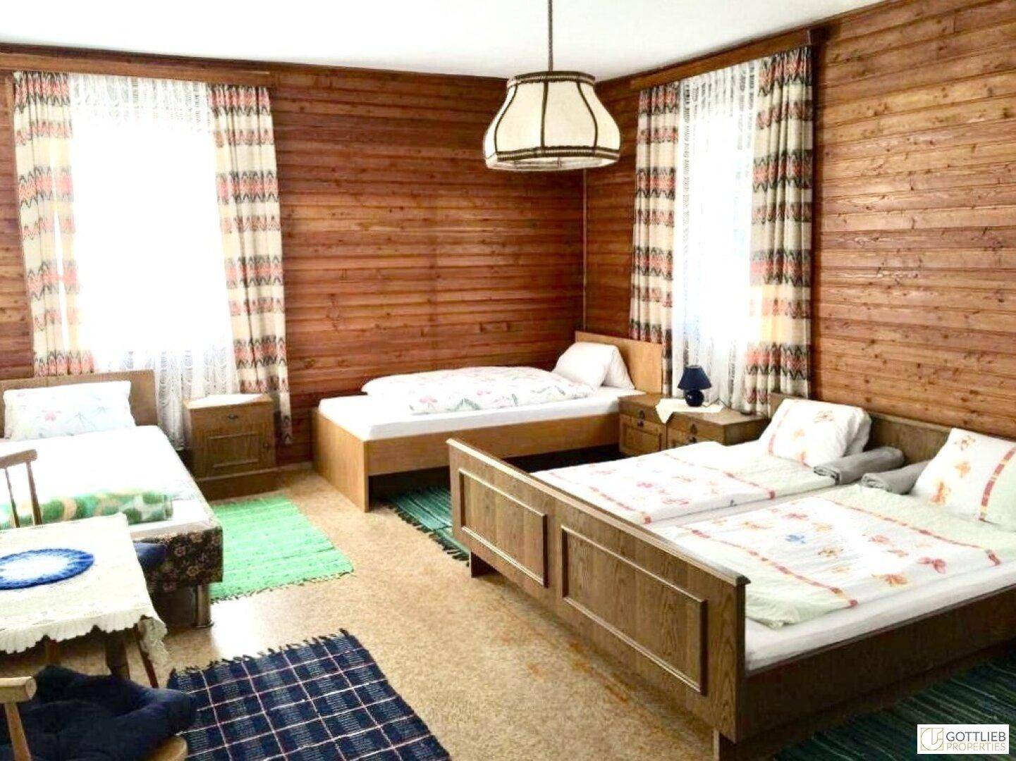 Rustikales Schlafzimmer mit Holzwänden, mehreren Betten und Teppichen, bietet eine traditionelle Einrichtung.