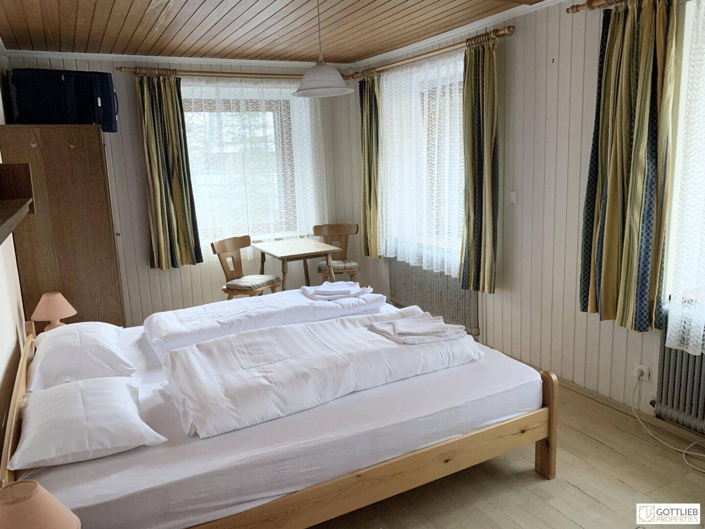 Helles Schlafzimmer mit zwei Einzelbetten, Holzboden und Fenstern mit Vorhängen.