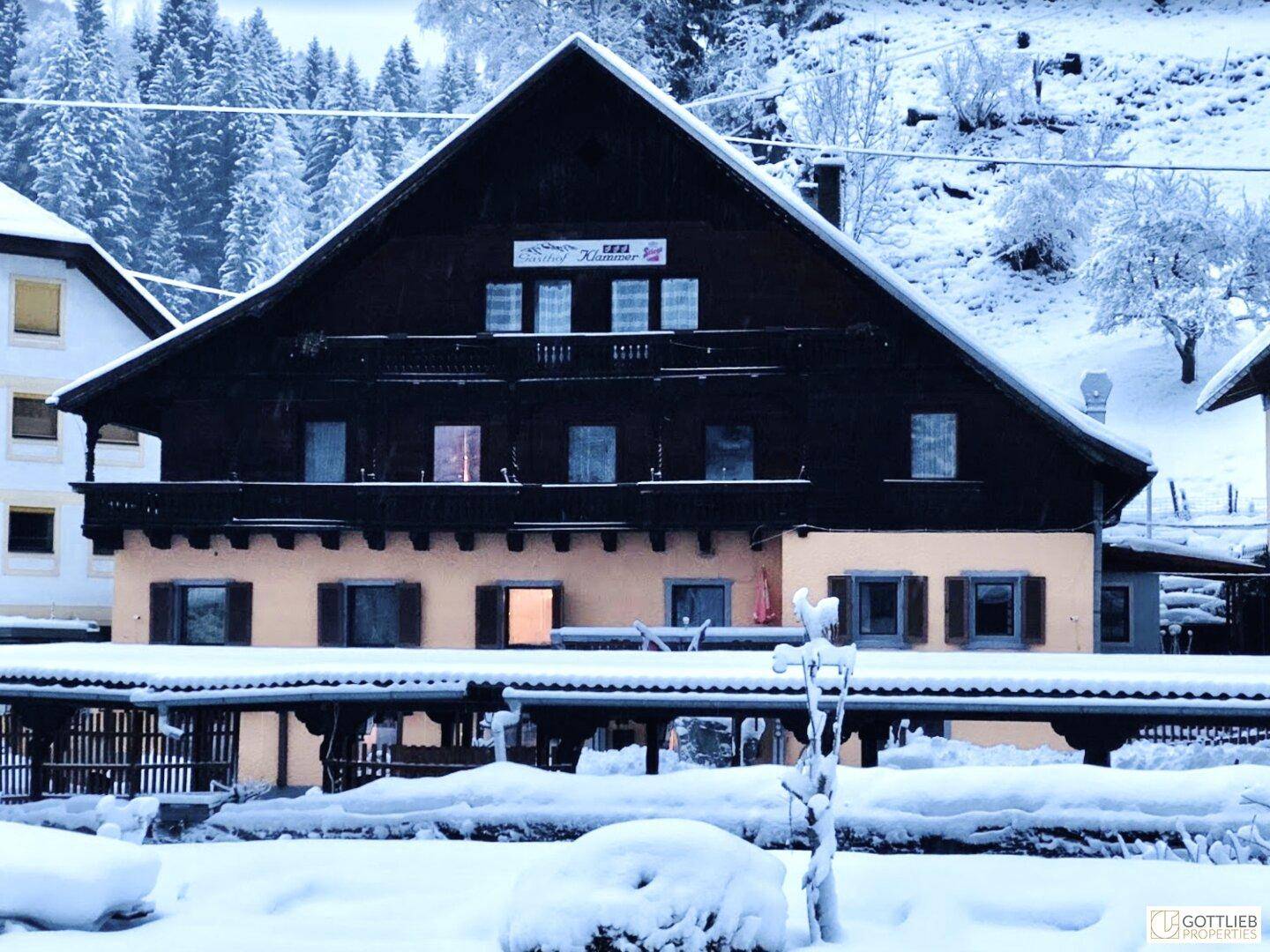 Traditionelles Gebäude mit dunkler Holzfassade und Balkonen, umgeben von Schnee im Winter, strahlt Gemütlichkeit aus.