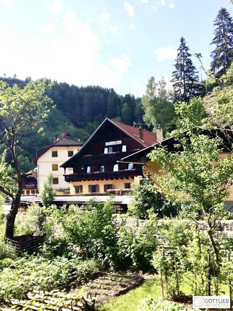 Traditioneller Gasthof mit Balkonen, umgeben von üppigem Grün und einem kleinen Gartenbereich, ideal zum Entspannen.