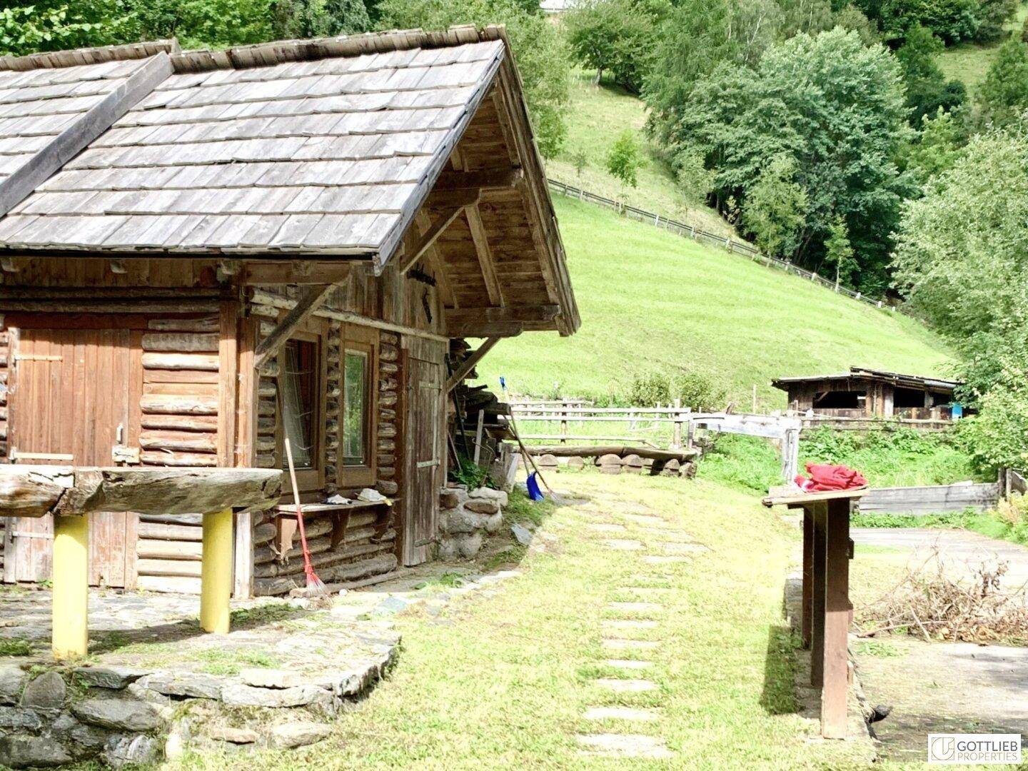 Rustikale Holzhütte mit einem Steinweg im Garten, umgeben von grünen Hügeln, bietet eine idyllische Atmosphäre.