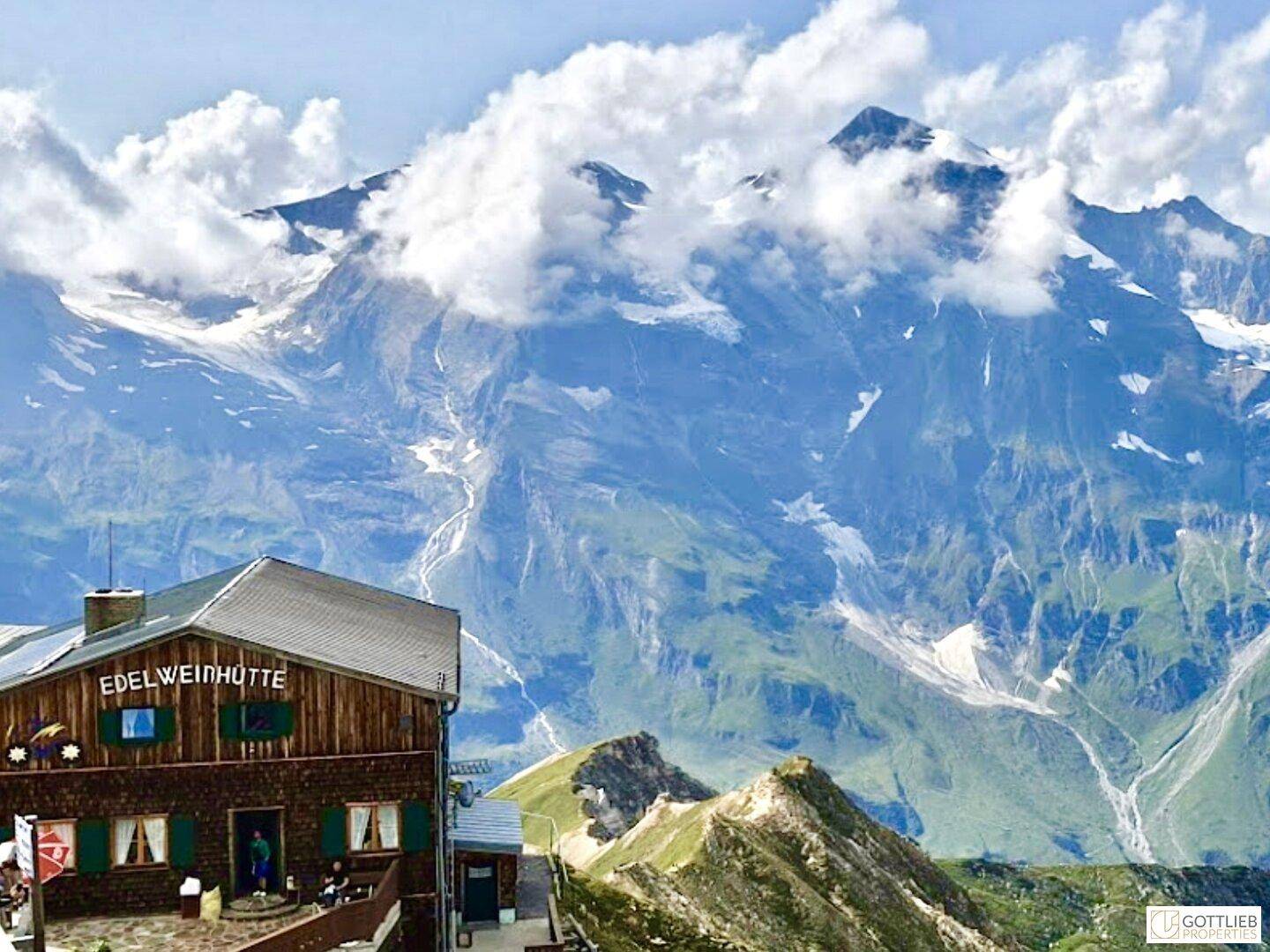 Eine Berghütte vor der beeindruckenden Kulisse schneebedeckter Gipfel und blauer Himmel, ein atemberaubender Ausblick.