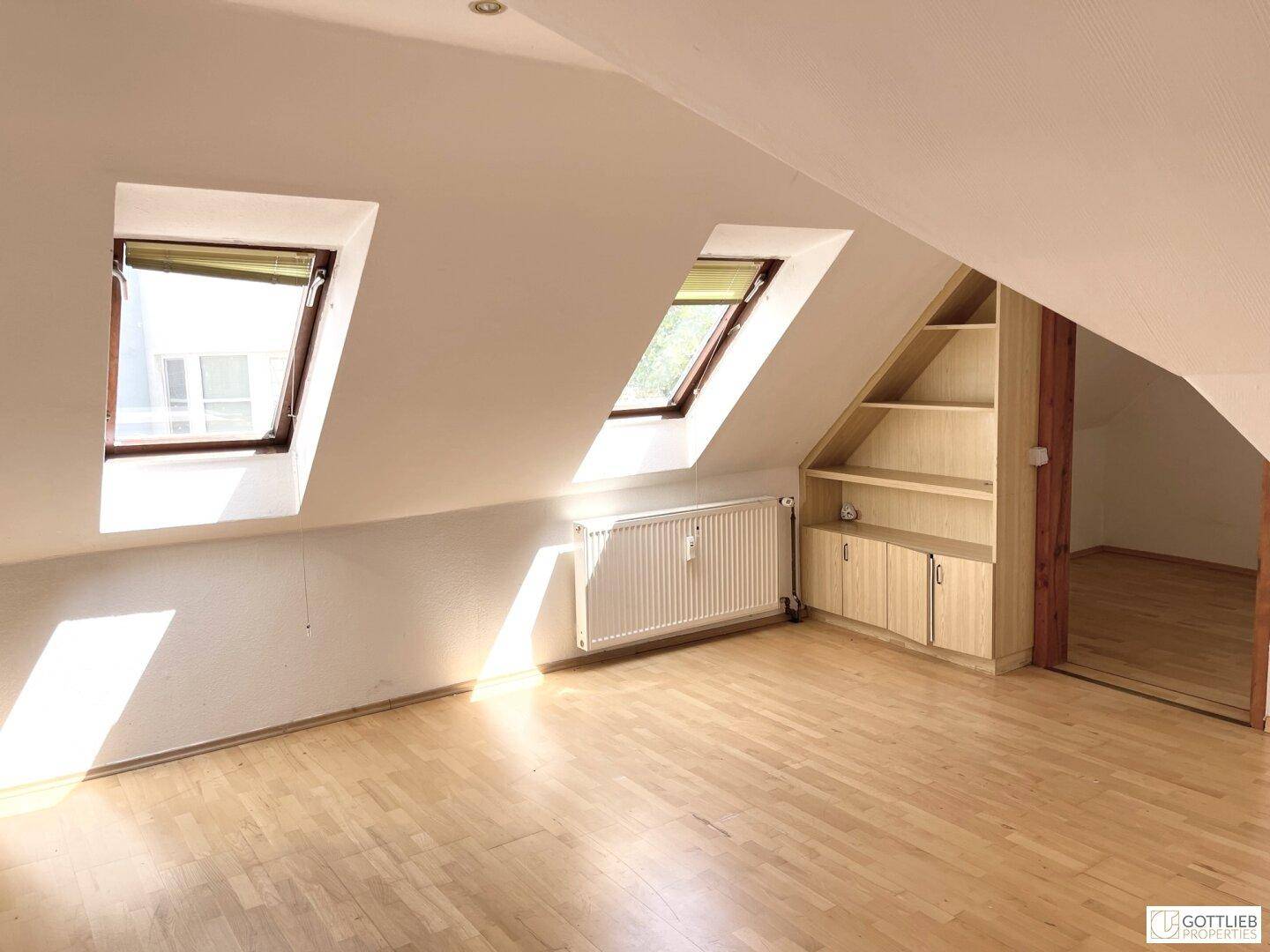 Dachgeschosszimmer mit zwei Dachfenstern, Holzboden und einem eingebauten Regal, das viel Stauraum bietet.