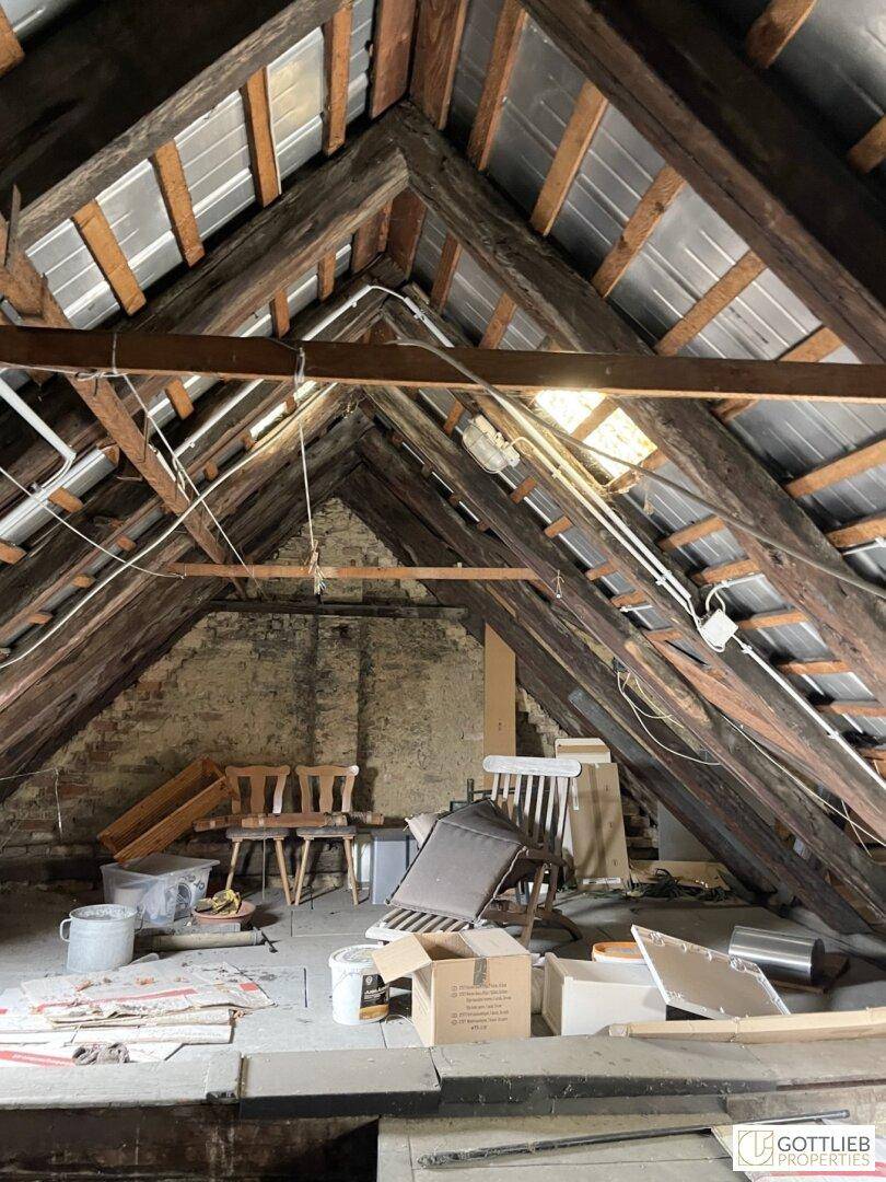 Ein ungenutzter Dachboden mit sichtbaren Holzbalken und Dachkonstruktion, der Renovierung benötigt.