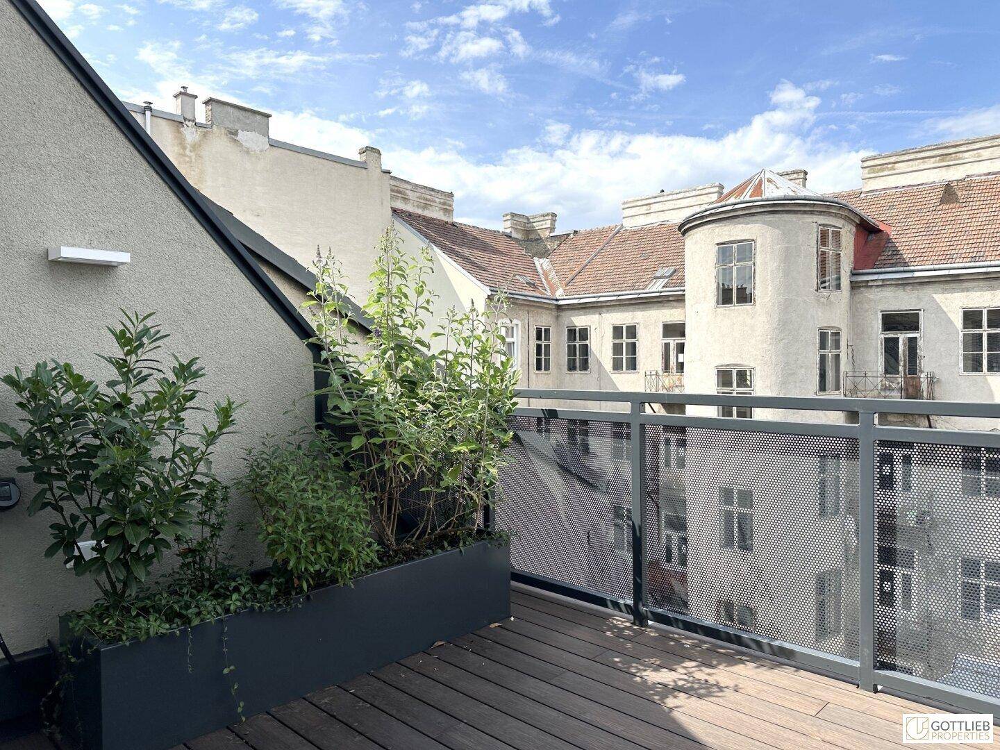 Geräumige Terrasse mit Holzboden, Pflanzen und Blick auf die umliegenden Gebäude der Stadt.