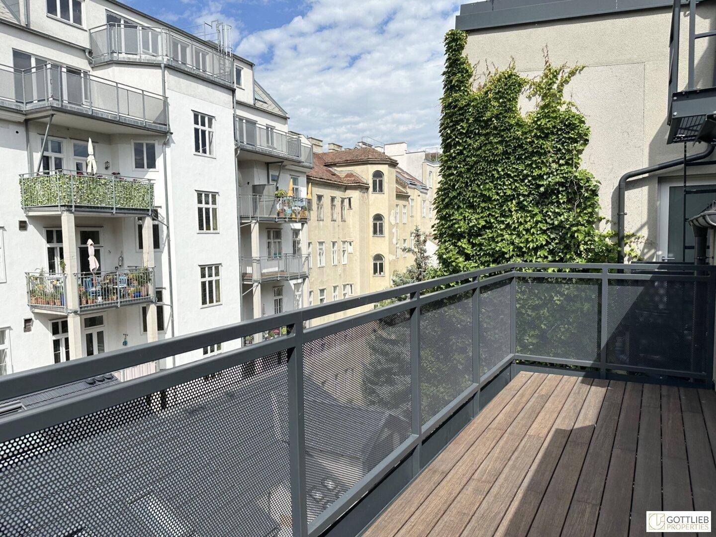 Moderne Terrasse mit Holzboden und Blick auf benachbarte Gebäude und grüne Fassaden.
